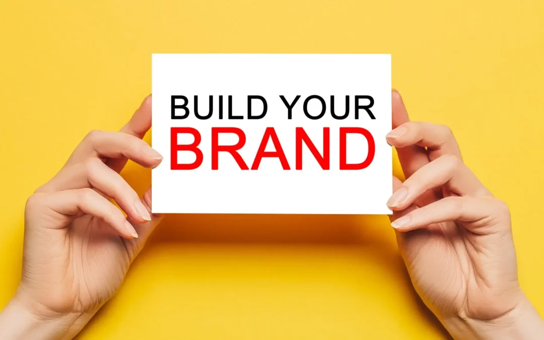 two hands holding an index card that has build your brand written on it.