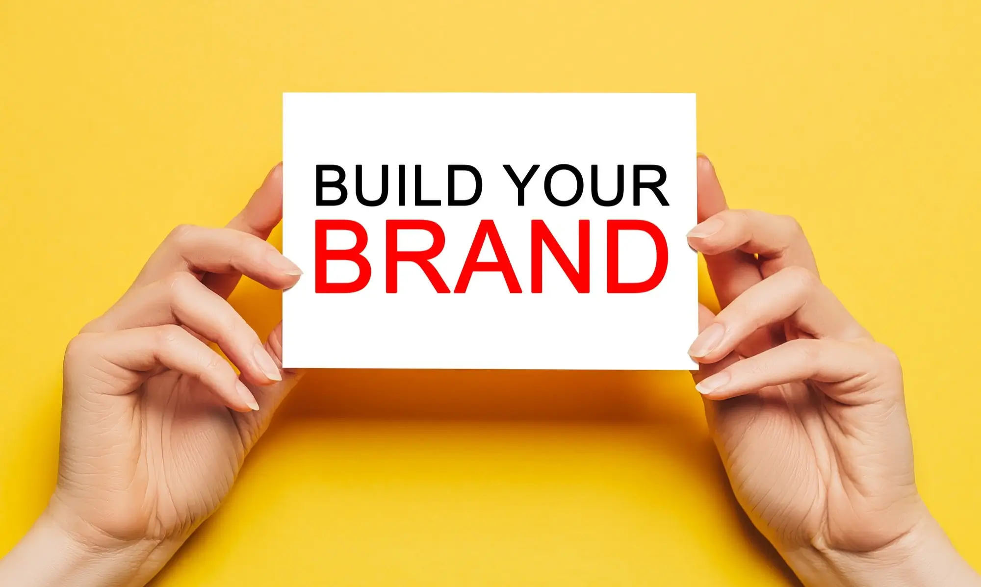 two hands holding an index card that has build your brand written on it.