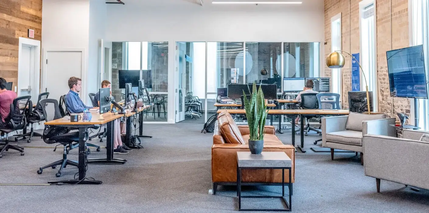 about-digital an open workspace with people on desks using computers and with empty chairs and desks.